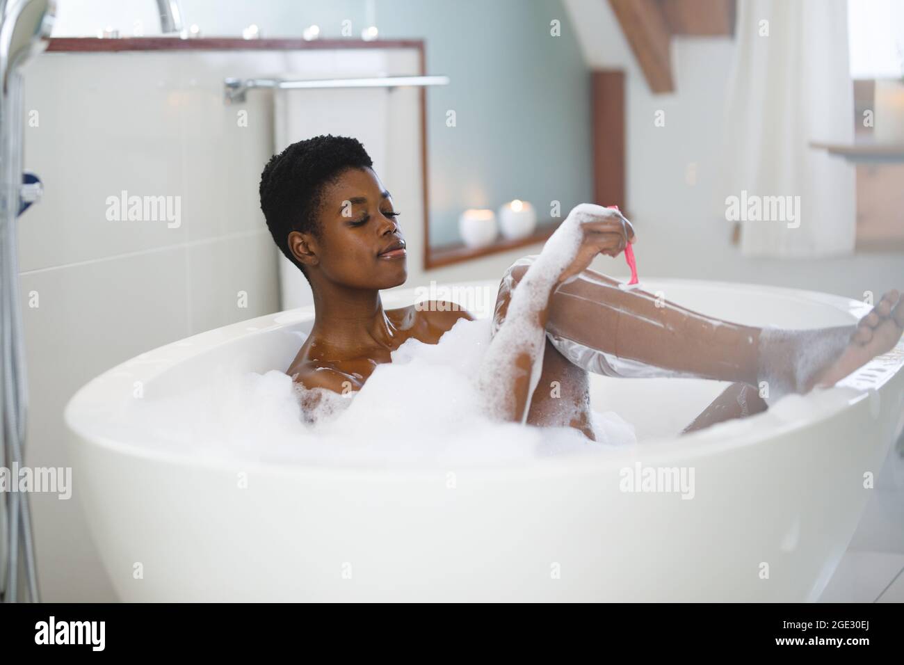 Smiling african american woman having foam bath and shaving her legs Stock Photo