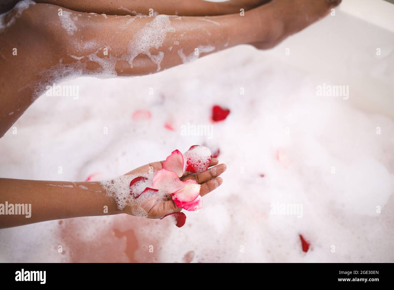 Close up of african american woman having pampering foam bath, adding rose petals Stock Photo