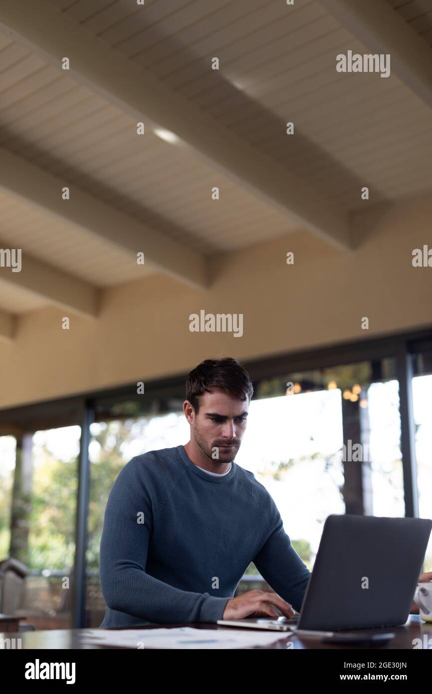 Caucasian man sitting at table and working remotely using laptop Stock Photo