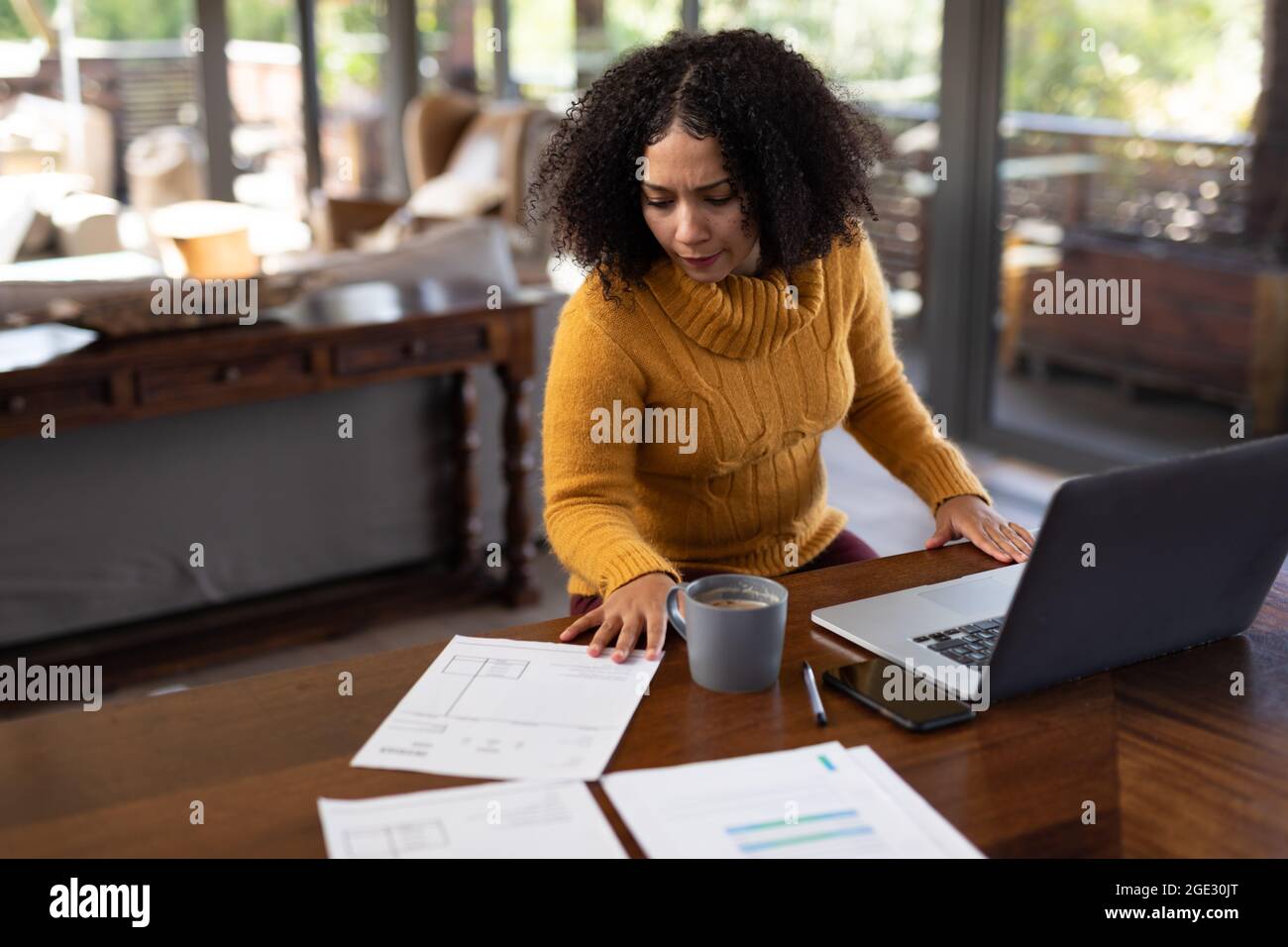 Mixed race woman sitting at table and working remotely using laptop Stock Photo