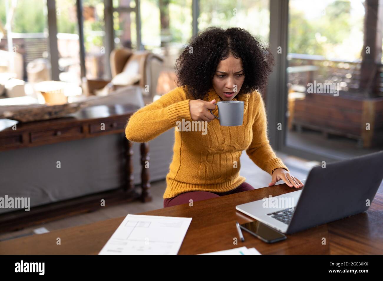 Mixed race woman sitting at table and working remotely using laptop Stock Photo