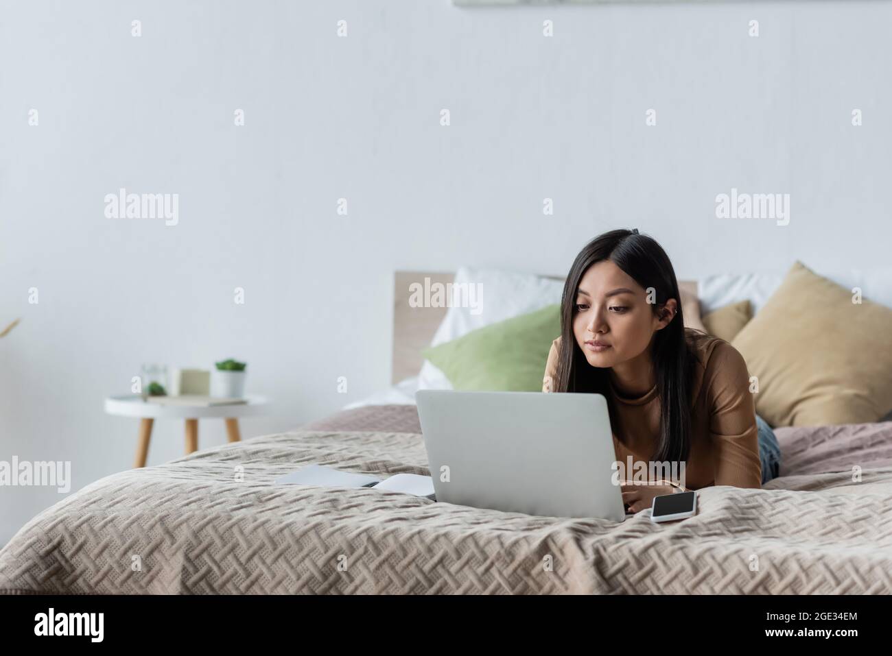 brunette asian woman using laptop while lying on bed at home Stock ...