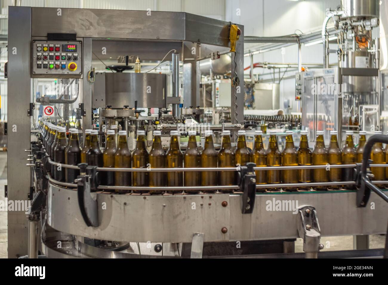 Brown glass bottles of drinking water on a conveyor belt move into a labeling machine. Food production Stock Photo