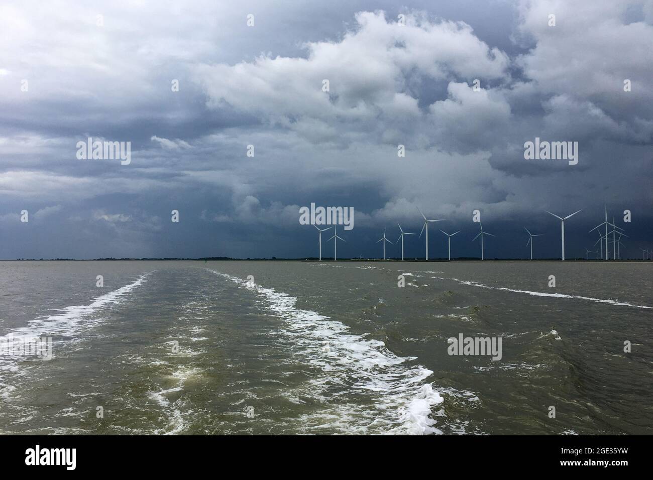 River Ems Mouth between Germany and Netherland with the Dutch Coast near Delfzijl with wind turbines a storm approaching. Shot from a boat. Stock Photo