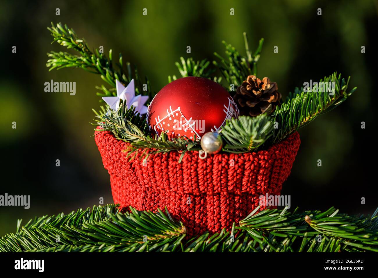 A red crocheted basket with fir branches and a red Christmas tree ball against a green background Stock Photo