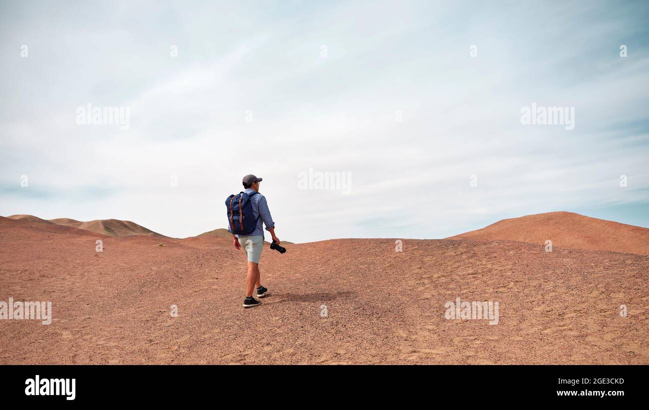 asian male backpacker landscape photographer walking on a hill looking at view, rear view Stock Photo