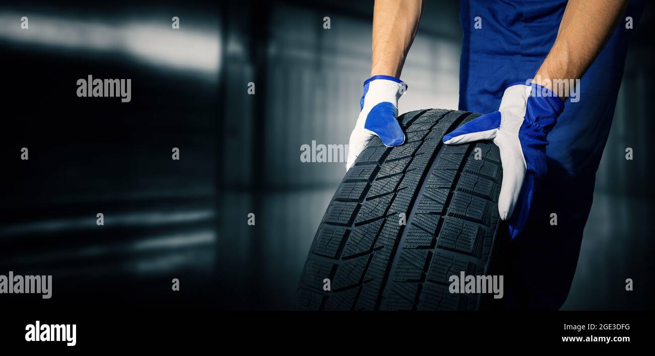 car tire shop and service - mechanic holding new tyre on garage background. copy space Stock Photo