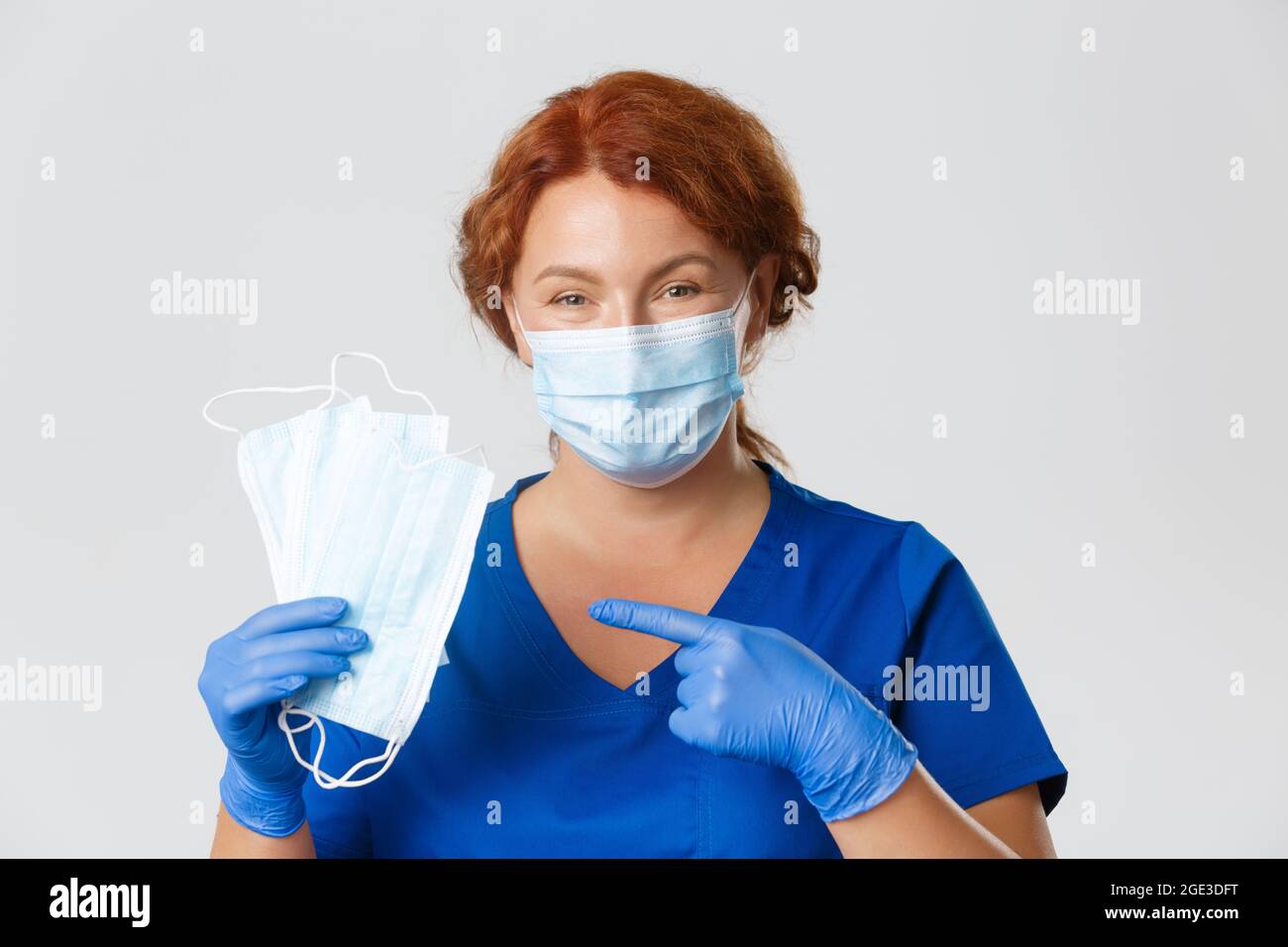 Medical workers, covid-19 pandemic, coronavirus concept. Close-up of smiling caring female nurse, doctor in rubber gloves pointing at face masks, ask Stock Photo