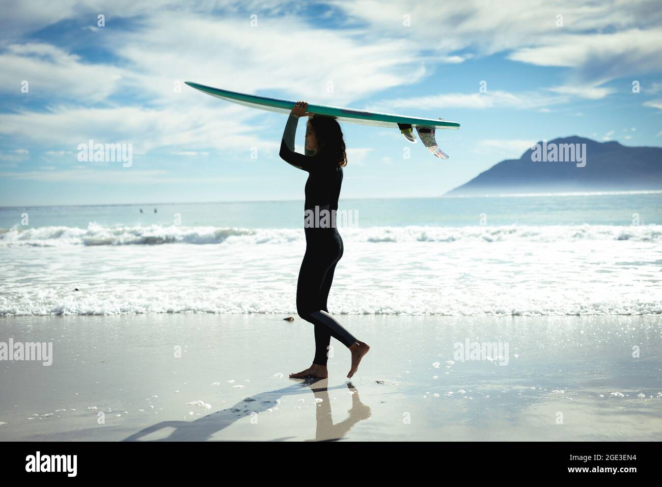 Mixed race woman holding surfboard on sunny day at beach Stock Photo