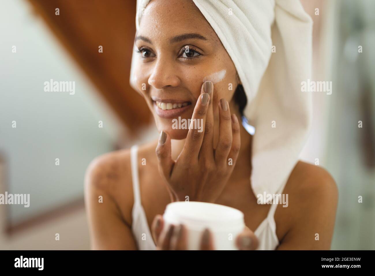Mixed race woman in bathroom applying face cream for skin care, smiling
