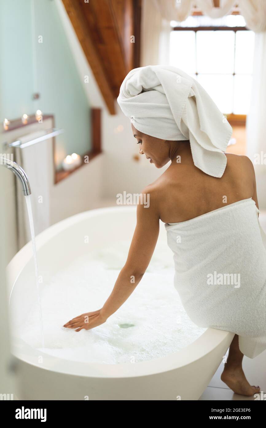 Mixed race woman in bathroom running a bath, sitting on the edge of tub Stock Photo