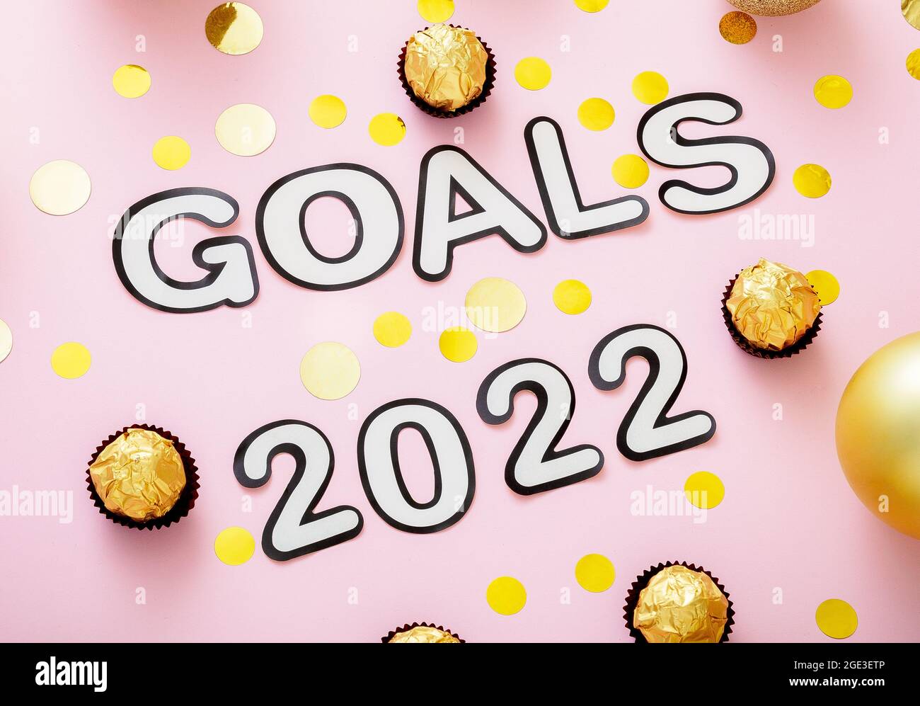 Goals 2022 lettering in Happy New Year style. 2020 Goals text with Christmas decorations gold confetti on pink color background. Stock Photo