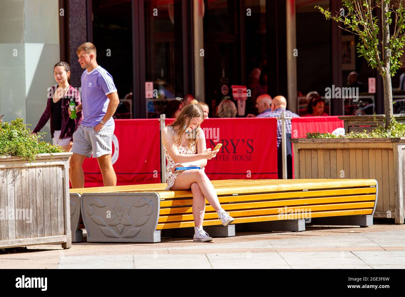 Dundee, Tayside, Scotland, UK. 16th Aug, 2021. UK Weather: A warm sunny day with a slight cool breeze across North East Scotland with temperatures reaching 20°C. A young woman sitting on a seat enjoying the warm sunshine whilst text messaging on her mobile phone and holding a Covid-19 self-test kit in Dundee city centre. Credit: Dundee Photographics/Alamy Live News Stock Photo