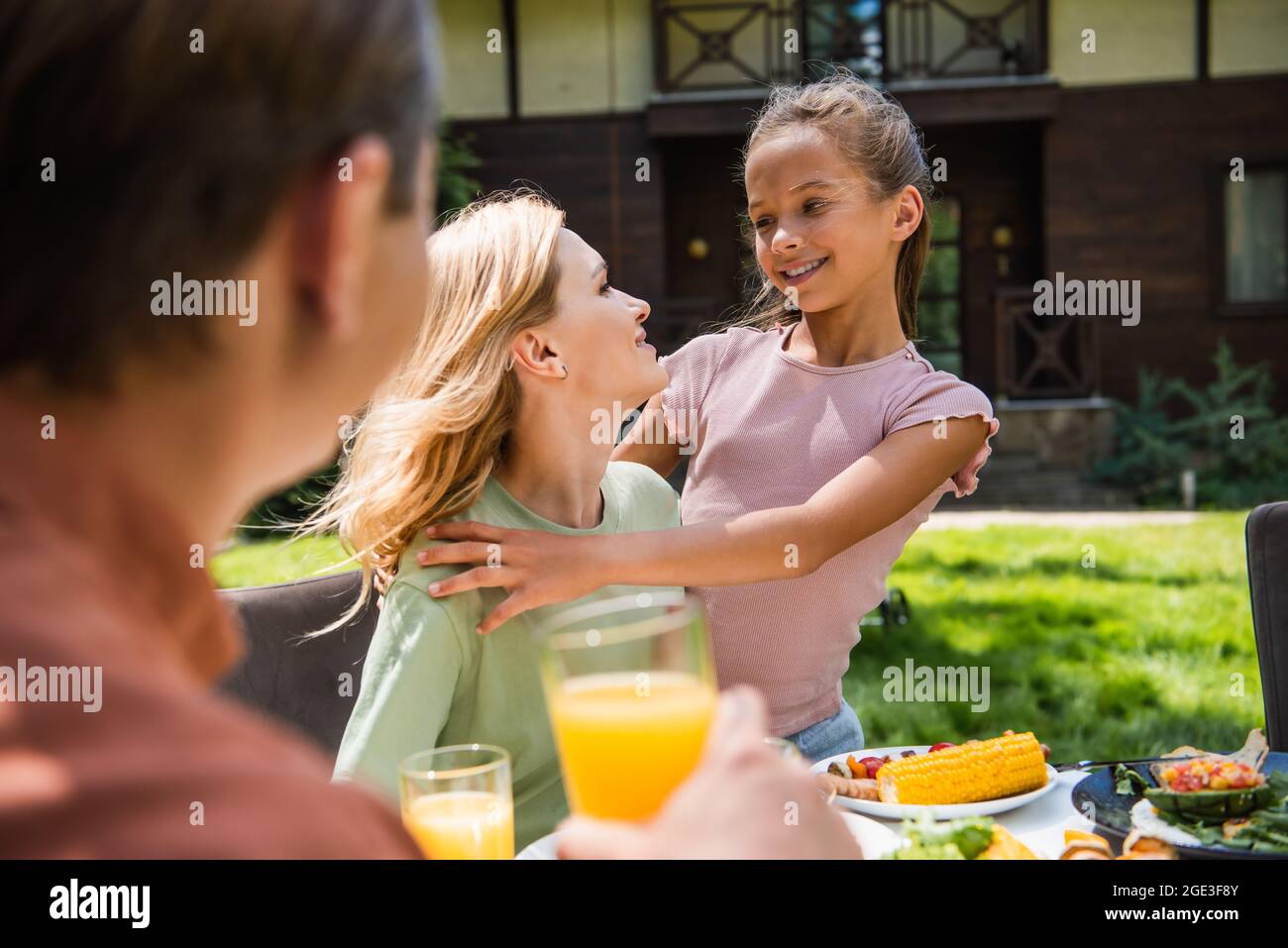 Smiling child hugging mother during picnic near blurred father outdoors Stock Photo