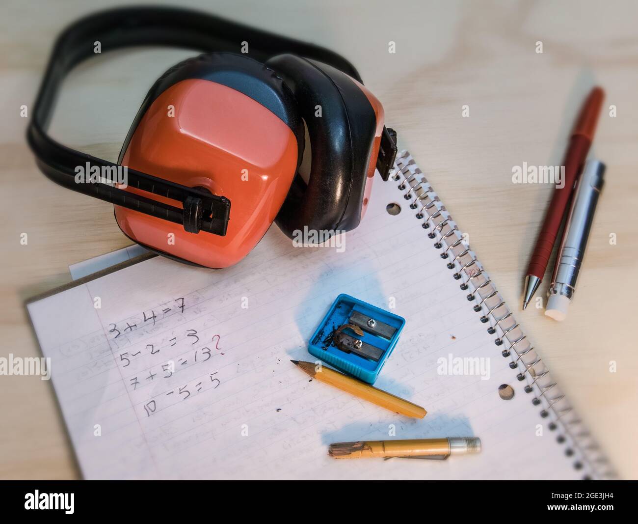 on a wooden table, a math exercise book, a broken pencil, a sharpener. On the other side of the table, a red correction pen and a chalk holder. Stock Photo