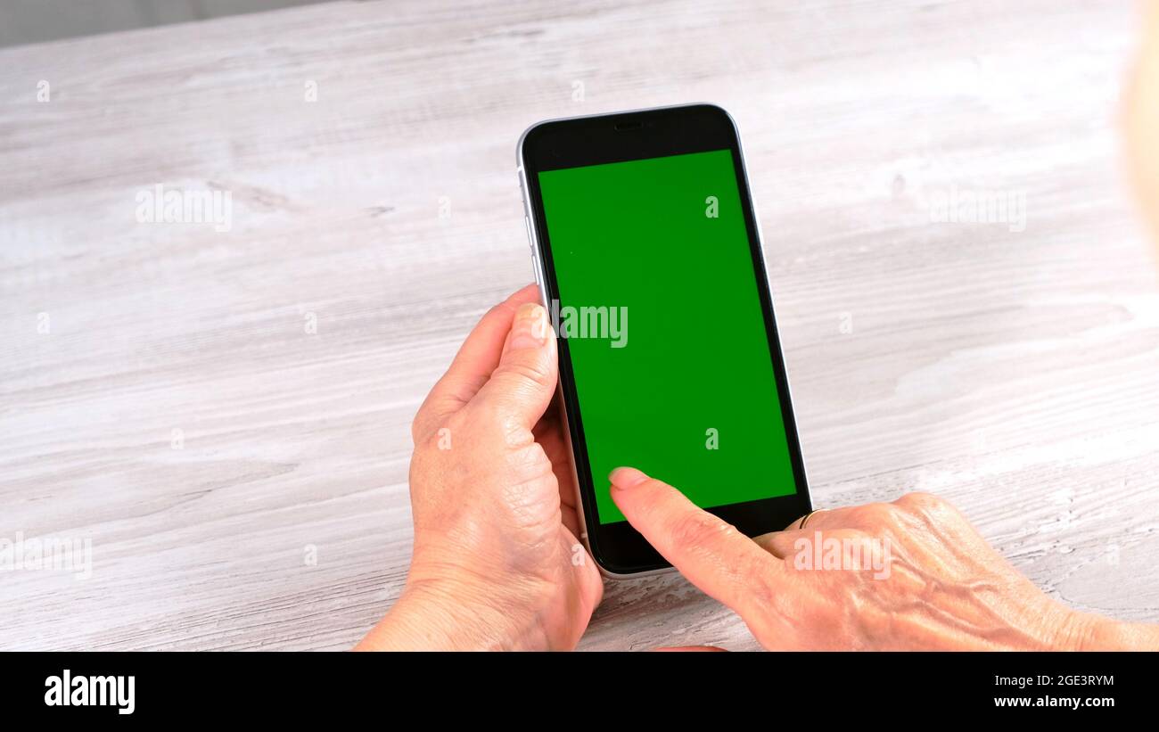 contactless in new normal concept from woman middle aged senior hold and use smart phone with green screen: Moscow, Russia - June 24, 2021. Stock Photo