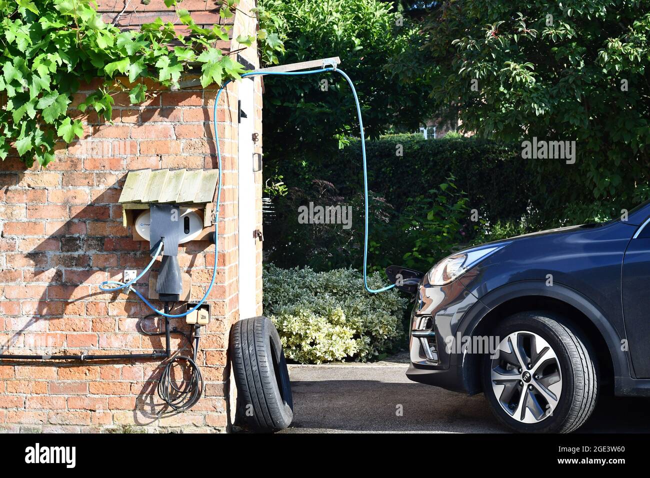 Rural Electric Car Charging point charging a fully electric car on a rural driveway with bespoke car charge housing, EV electric car charging point Stock Photo
