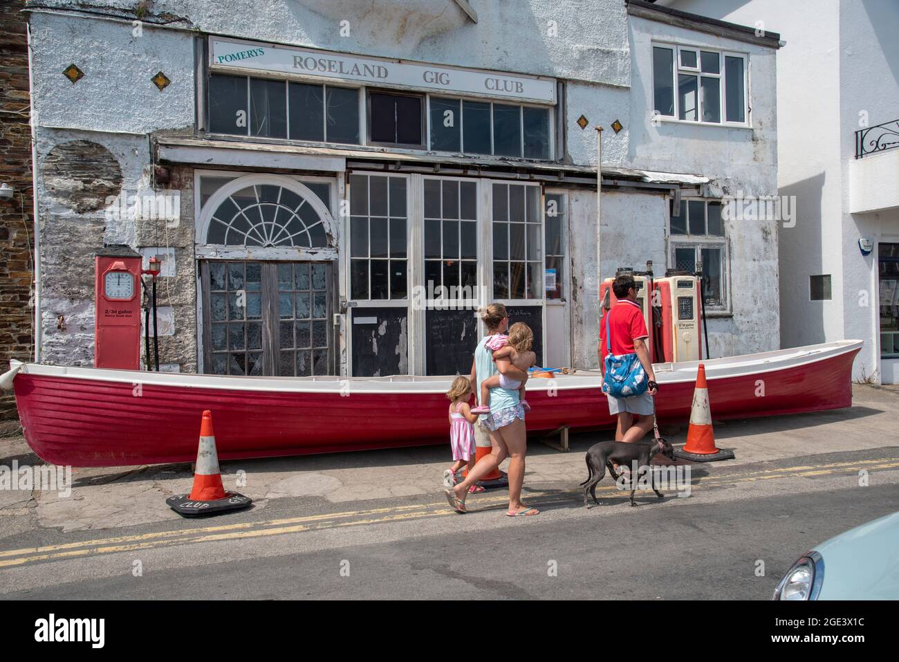 St Mawes, Cornwall, England, UK. Holidaymakers walking past the Roseland Gig Club formerly the Pomerys garage on the harbour front in St Mawes, Cornwa Stock Photo
