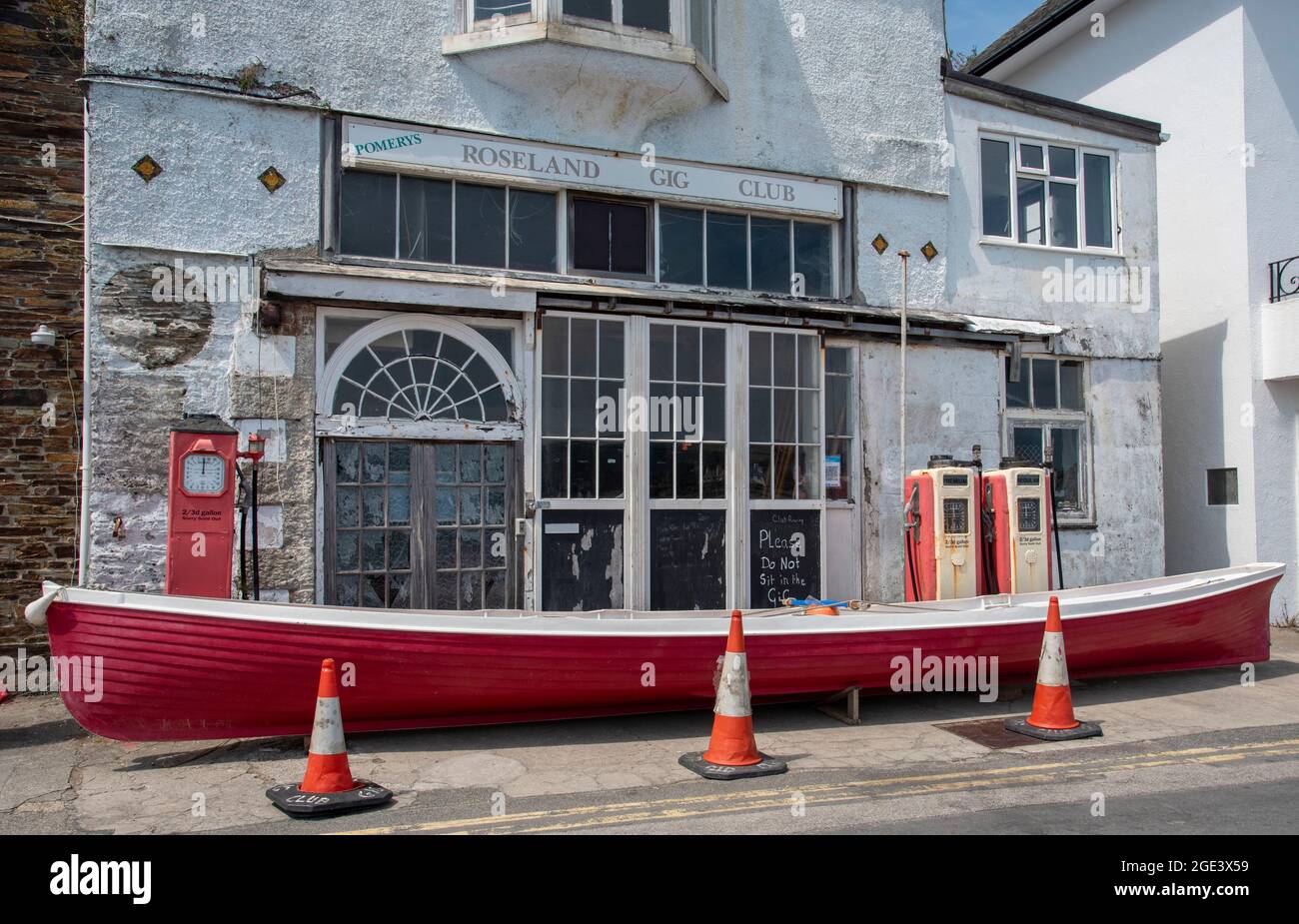 St Mawes, Cornwall, England, UK. A red and white painted gig stands outside the Roseland Gig Club formerly the Pomerys garage on the harbour front in Stock Photo