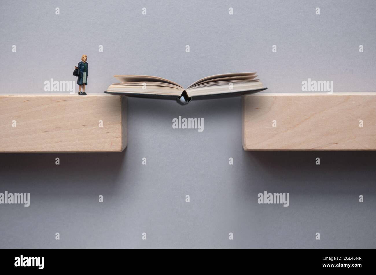 Open book bridging the gap between wooden blocks for female miniature figure to cross Stock Photo