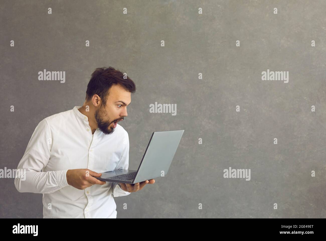 Young man shocked and surprised, looks at the laptop screen. Stock Photo