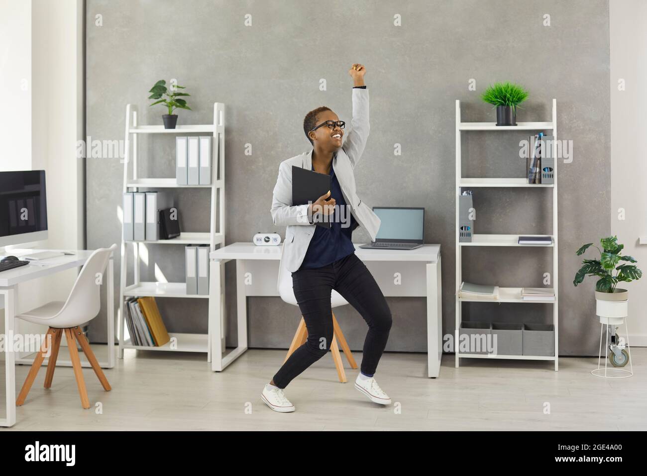 Funny happy excited young black business woman dancing and having fun in the office Stock Photo