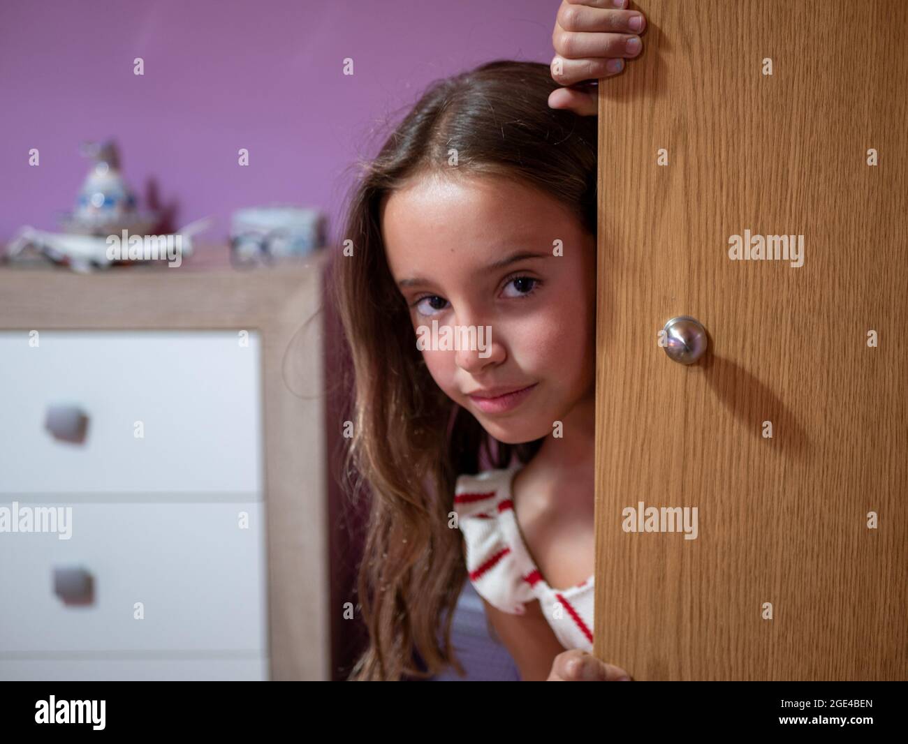 Cute little Caucasian girl looking from behind the wooden door of her
