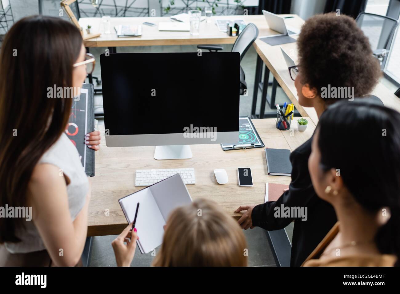 blurred multiethnic businesswomen near computer monitor with blank ...