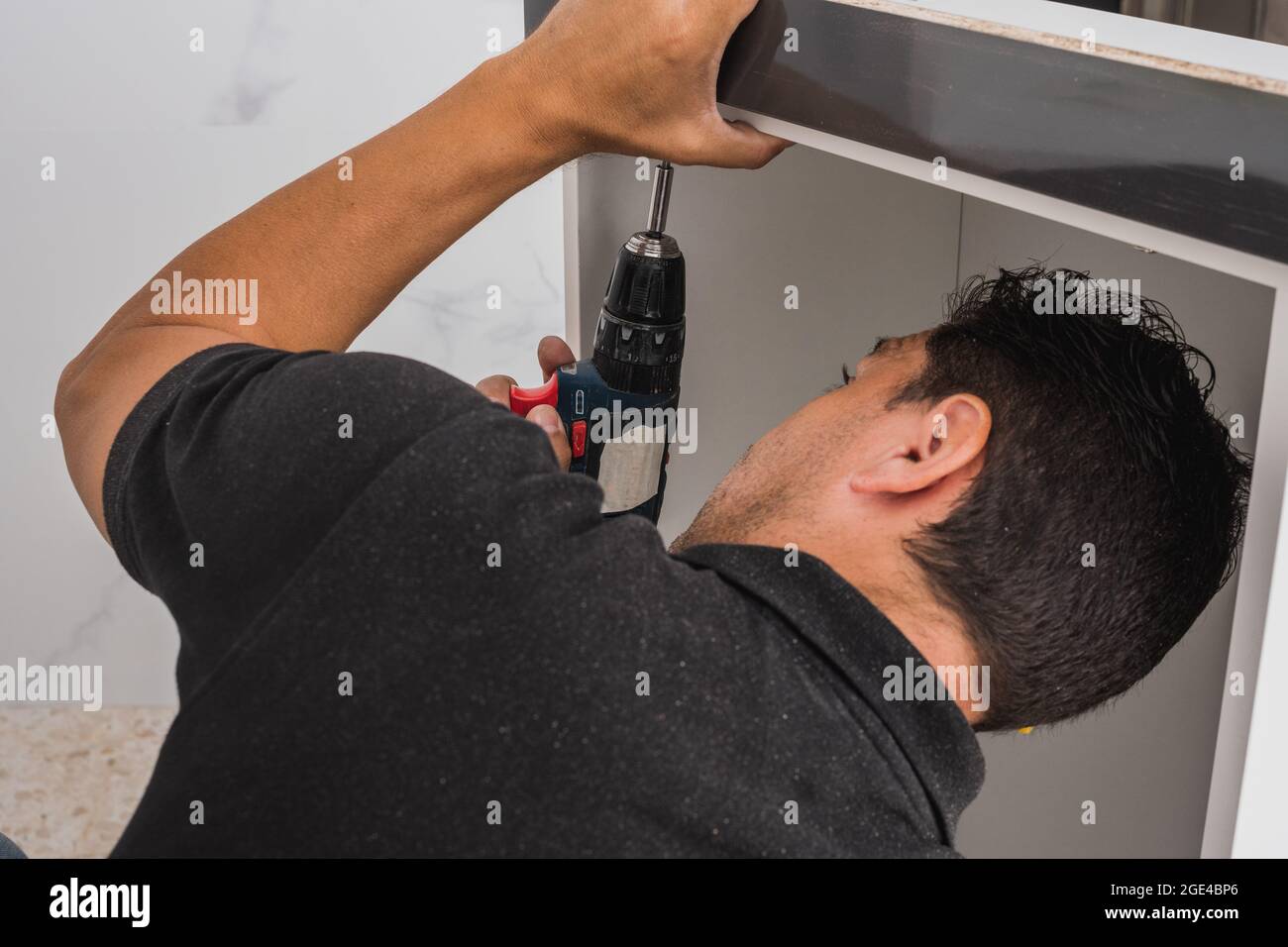 Man bent over while using a drill to assemble a kitchen unit Stock Photo