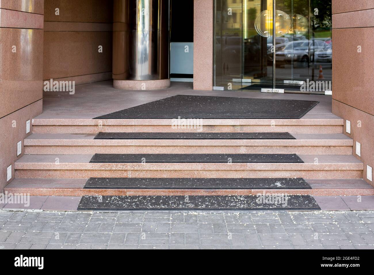 threshold with step with foot mat at entrance to store with tempered glass door in doorway tiled with granite and lighting on stairs front view, nobod Stock Photo