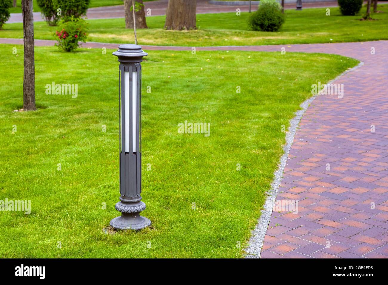 curved pedestrian pavement of stone tiles in park with landscape lighting and green plants bushes with trees, landscaped of on the lawn with ground ga Stock Photo
