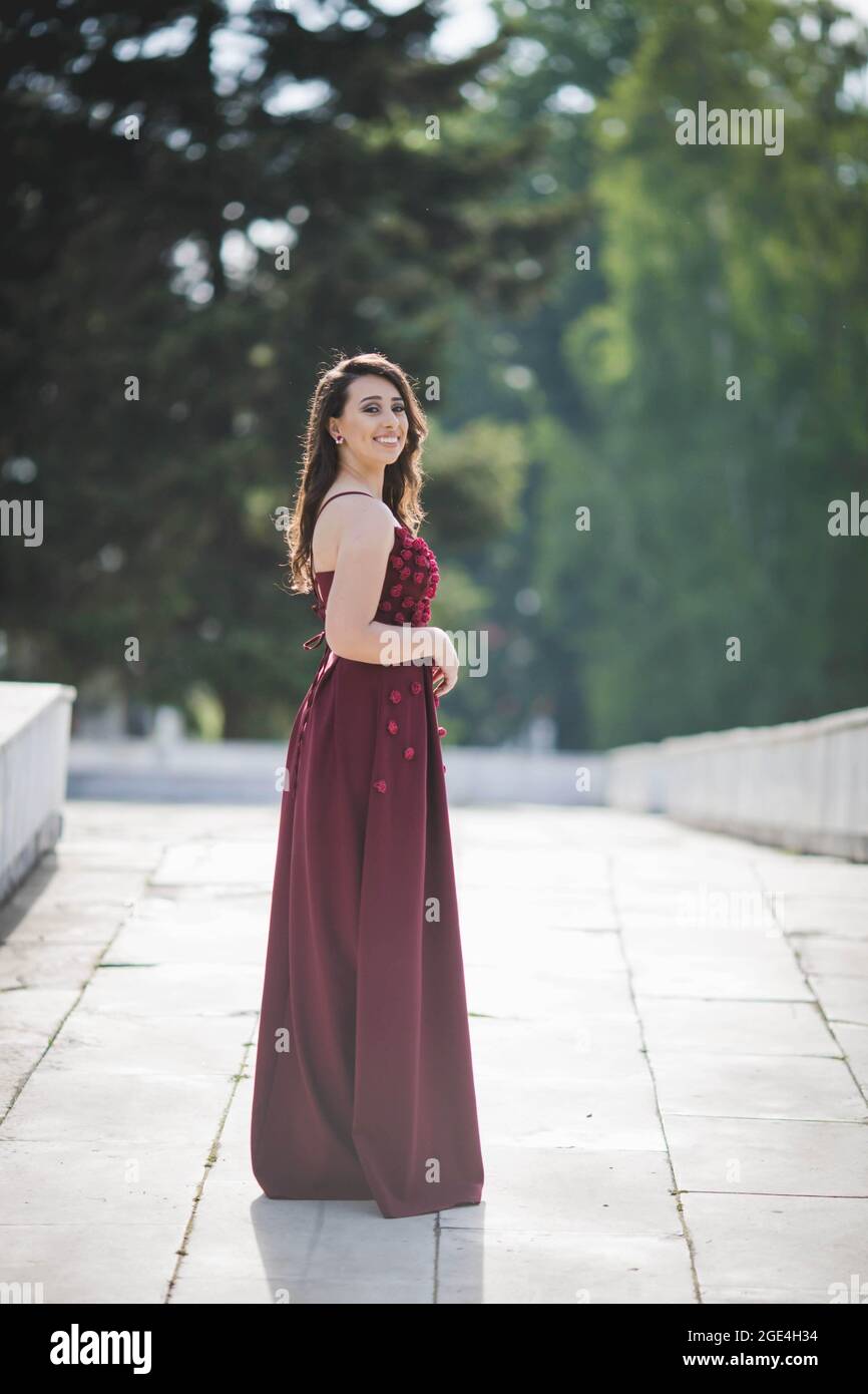 Closeup shot of a young woman posing in a red dress on a pathway and ...