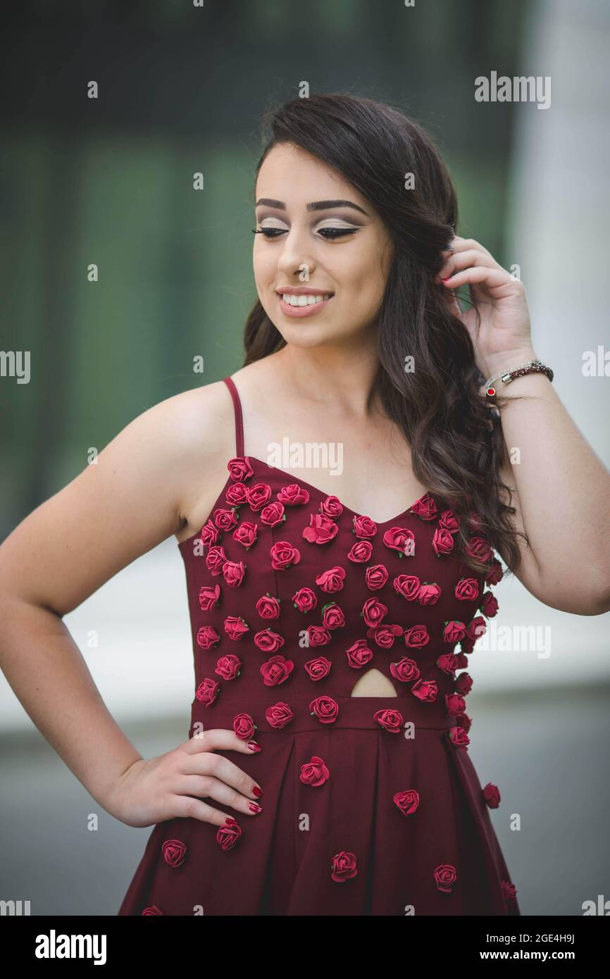 Vertical shot of a shy woman posing in a red flowery dress in front of