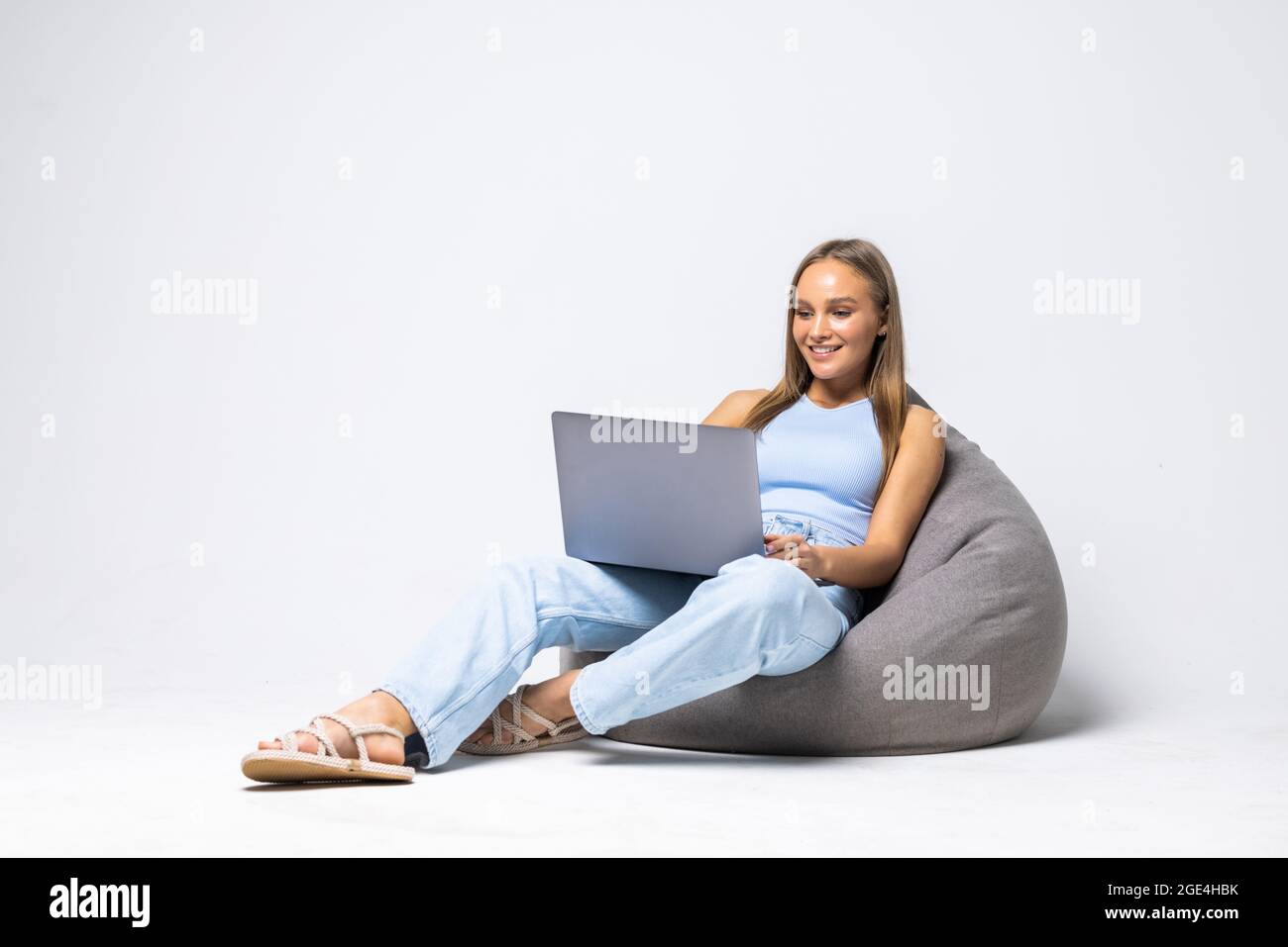 Beautiful girl is sitting on bean bag couch and is looking laptop on white background. Stock Photo