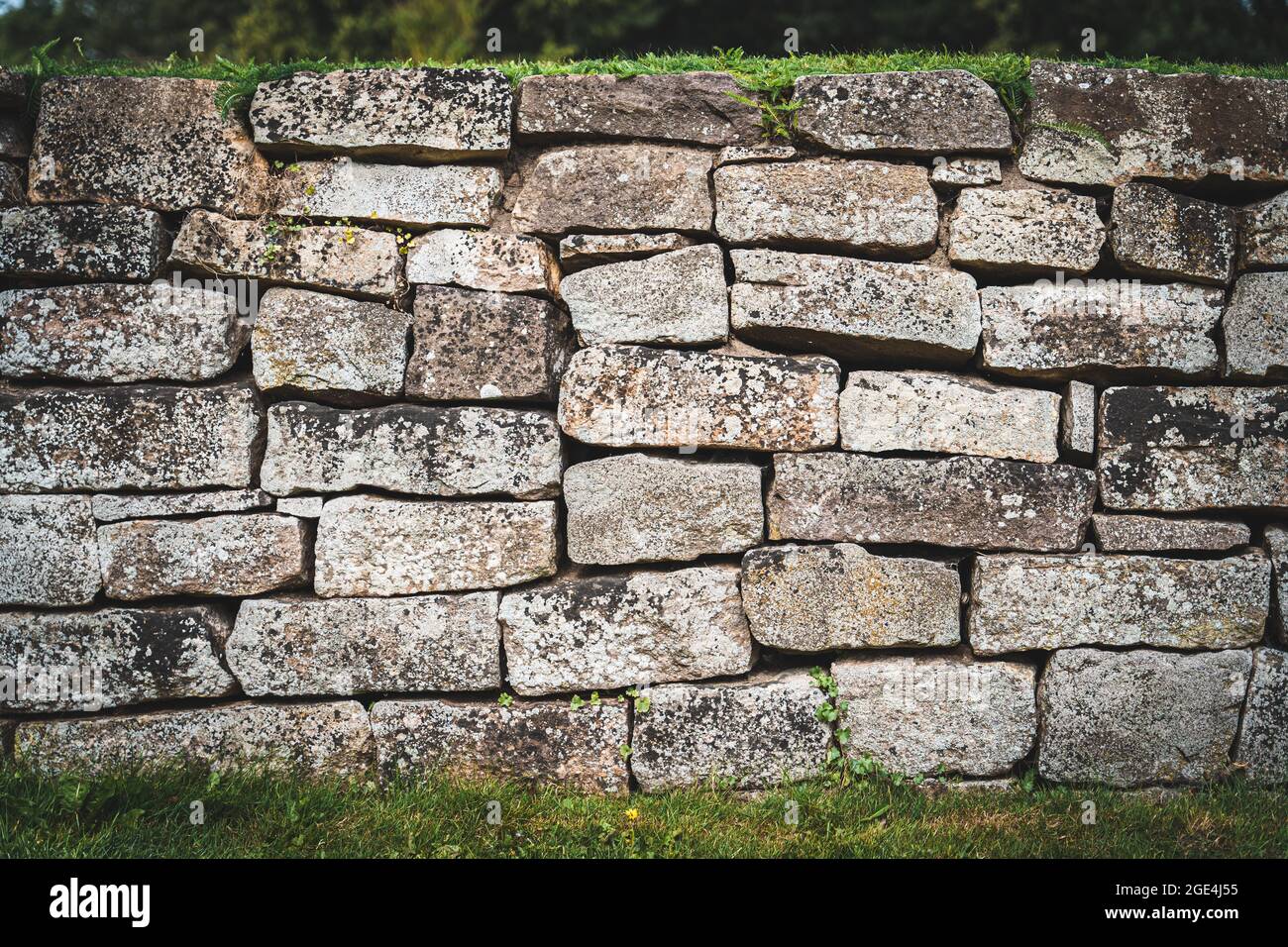 Old wall made of coarse stone framed by some green grass Stock Photo