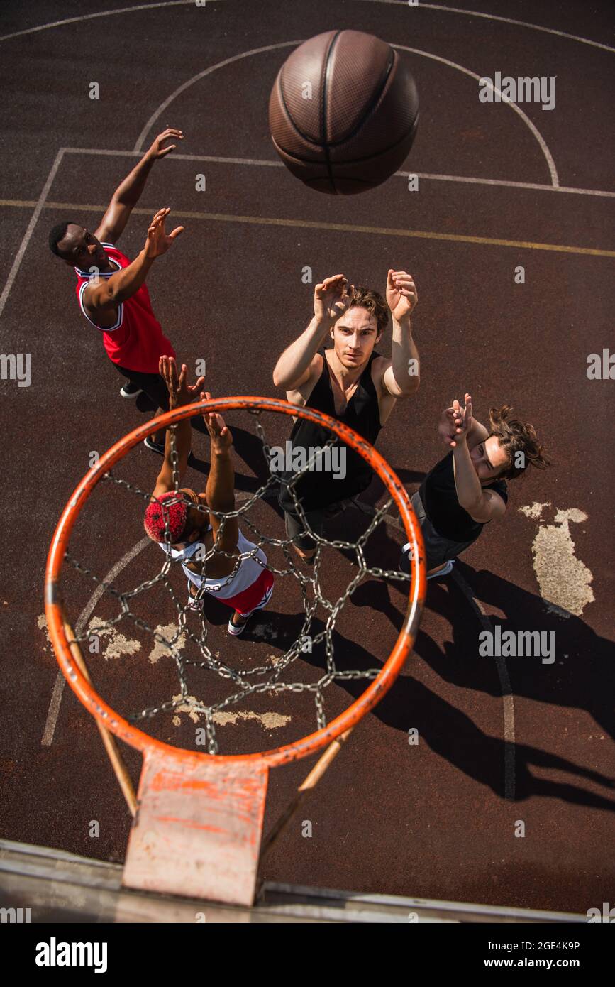 Overhead view of man throwing basketball ball near multiethnic friends with raised hands and