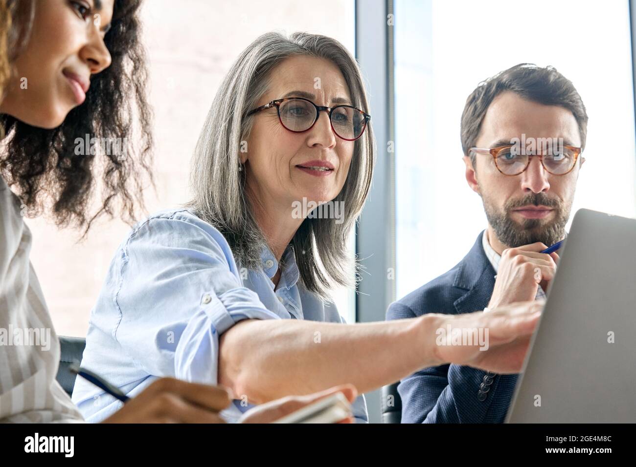 Diverse business executive team discuss corporate report using laptop at table. Stock Photo