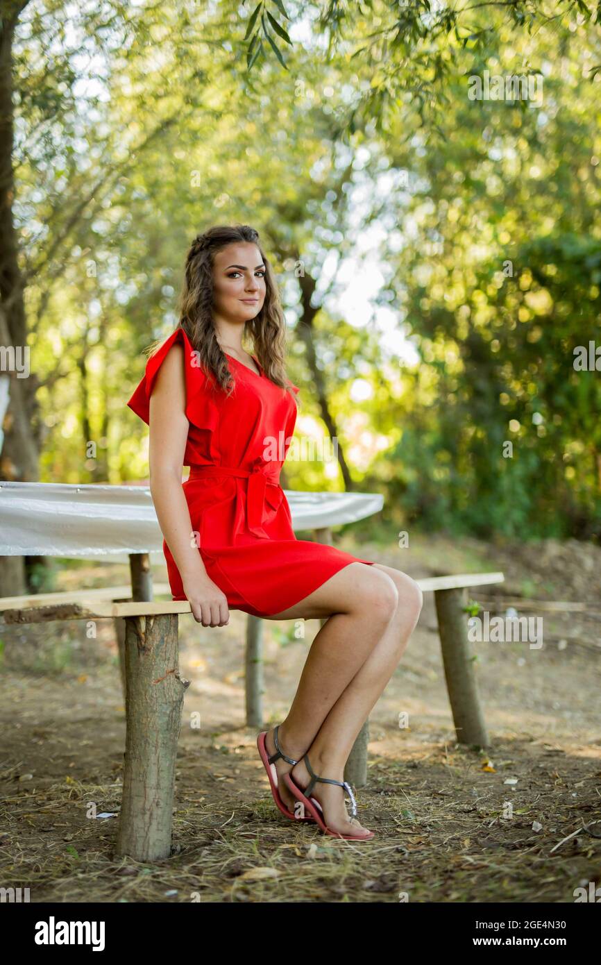 Shallow focus shot of a young woman sitting on a bench in a red dress ...
