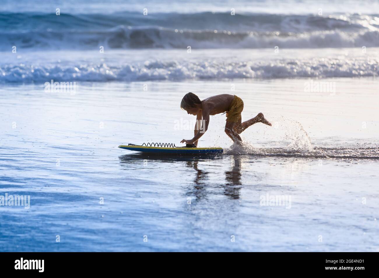 Happy boy. Young surfer with bodyboard have fun on beach, run by sea water pool. Active family lifestyle, kids outdoor water sports, swimming activity Stock Photo