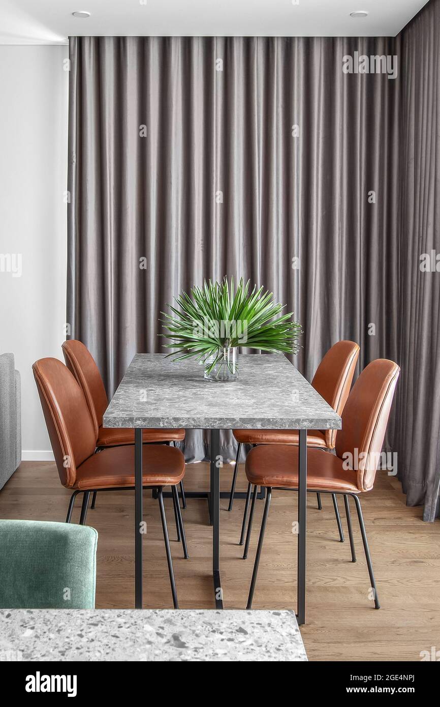 Grey Dining marble stone table with four rust leather chairs and grey curtains in Scandinavian minimalist dining room interior Stock Photo
