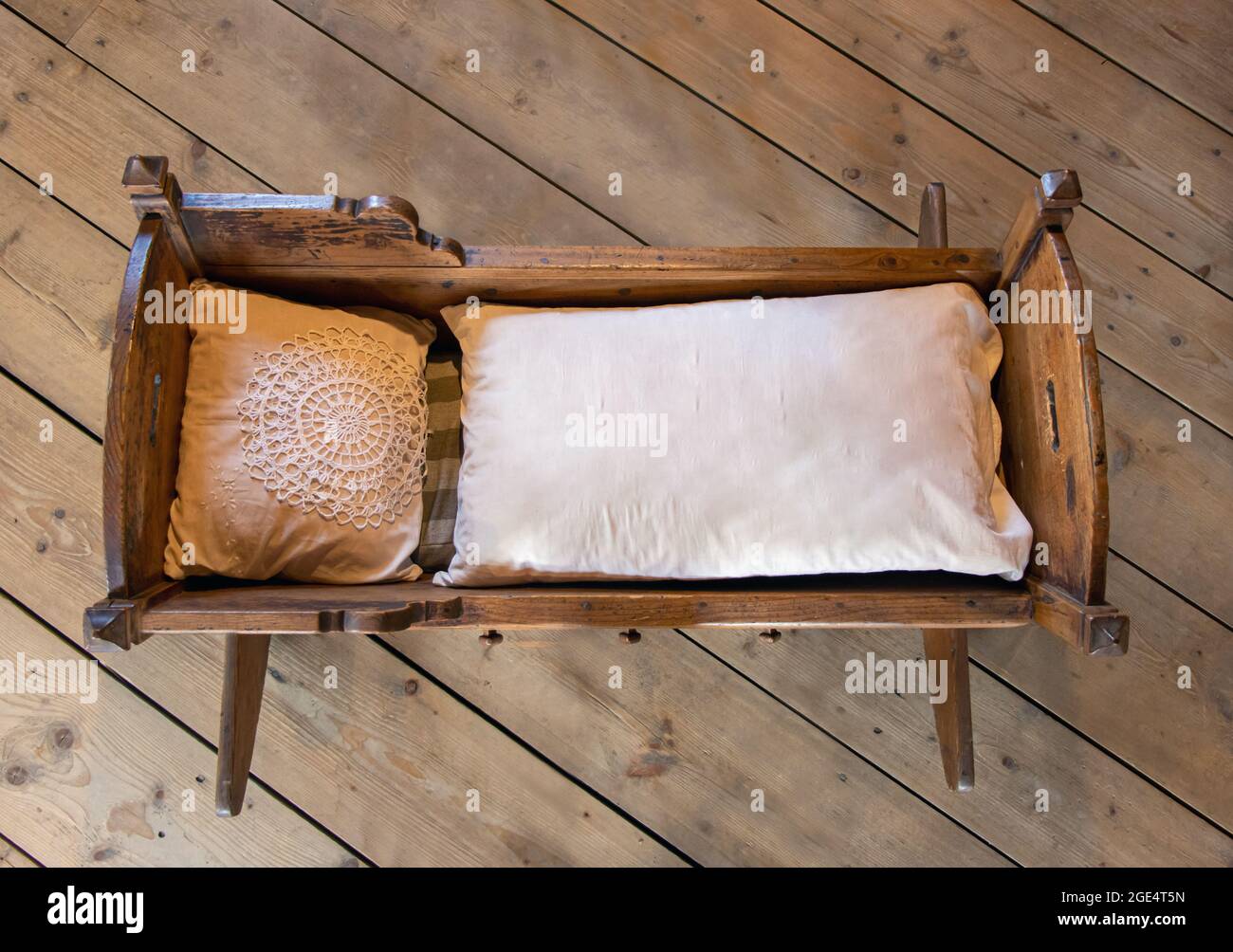 Old cradle with duvet and pillow on the wooden floor. Stock Photo