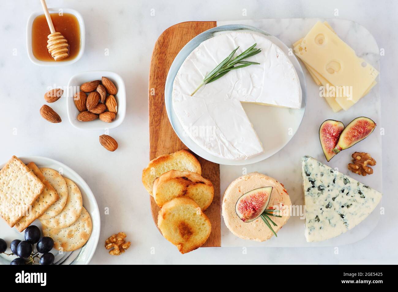 Cheese platter with a selection a cheeses, crackers, figs, nuts and honey. Overhead table scene on a bright background. Stock Photo