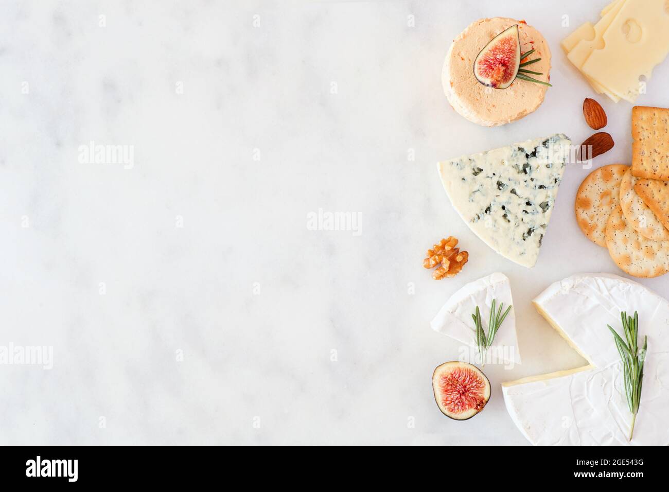 Border of a selection of cheeses, figs, nuts and crackers. Top view on a white marble background with copy space. Stock Photo