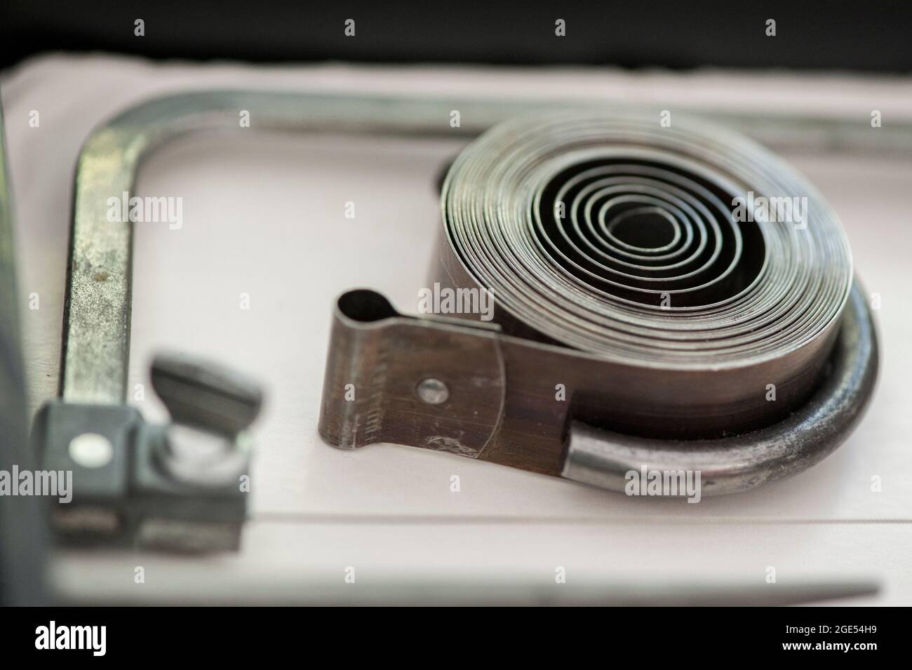 A cclamp restrains a clock mainspring, which is under high tension, to