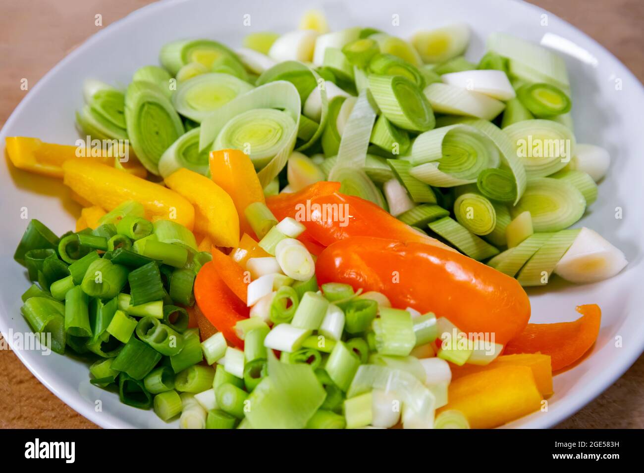Sliced leeks, peppers and spring onions in a white bowl Stock Photo