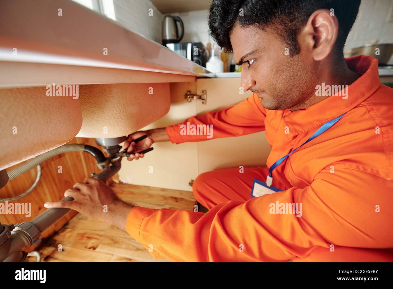 Serious handyman using pliers when fixing leaking pipe under sink in