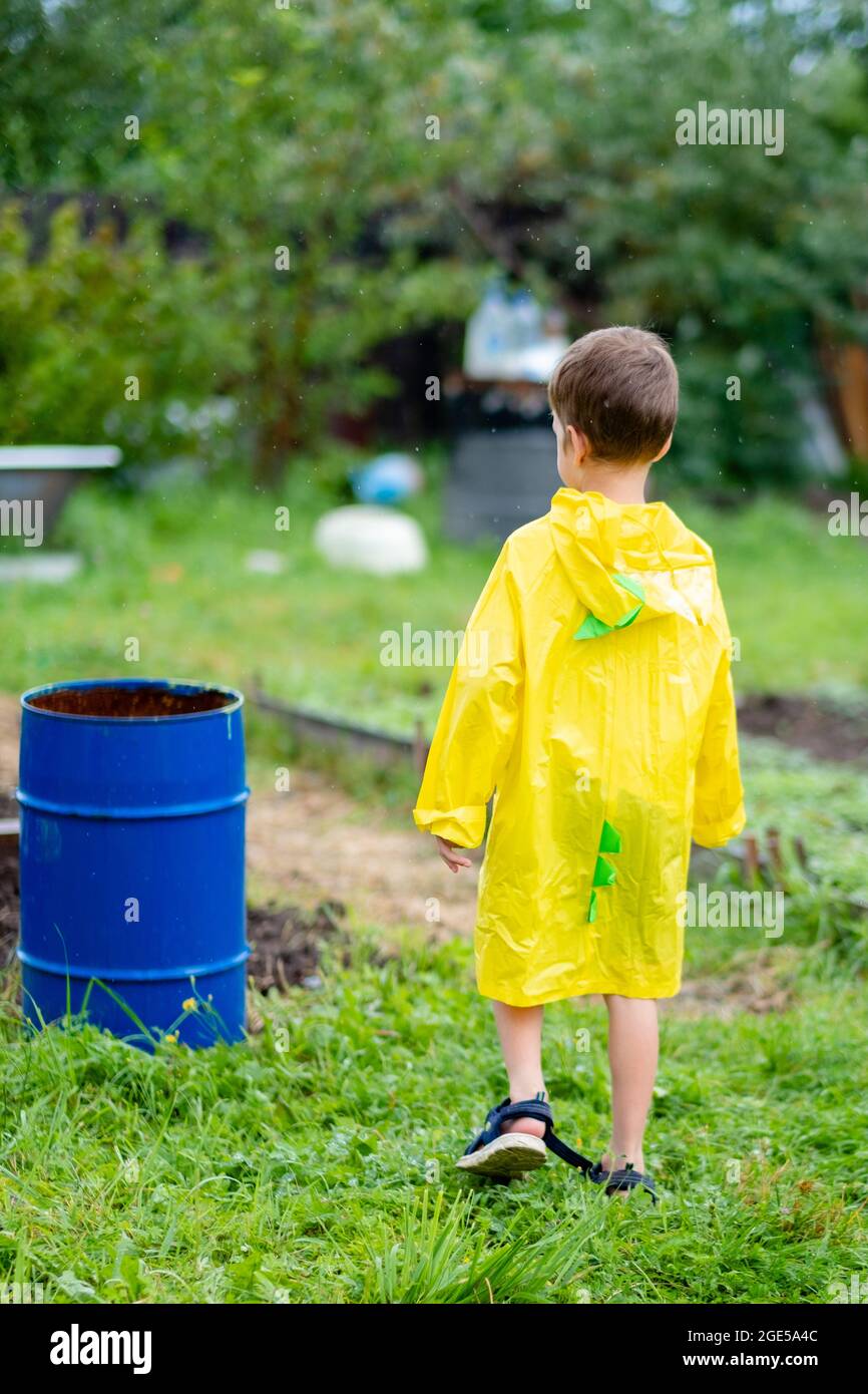 A boy in a yellow raincoat walks in the rain, back view. A child on the