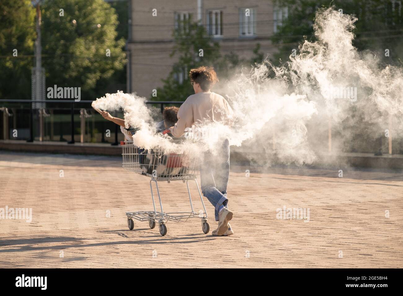 Ecstatic teenage dates having fun with firecrackers while guy pushing shopping cart with his girlfriend Stock Photo