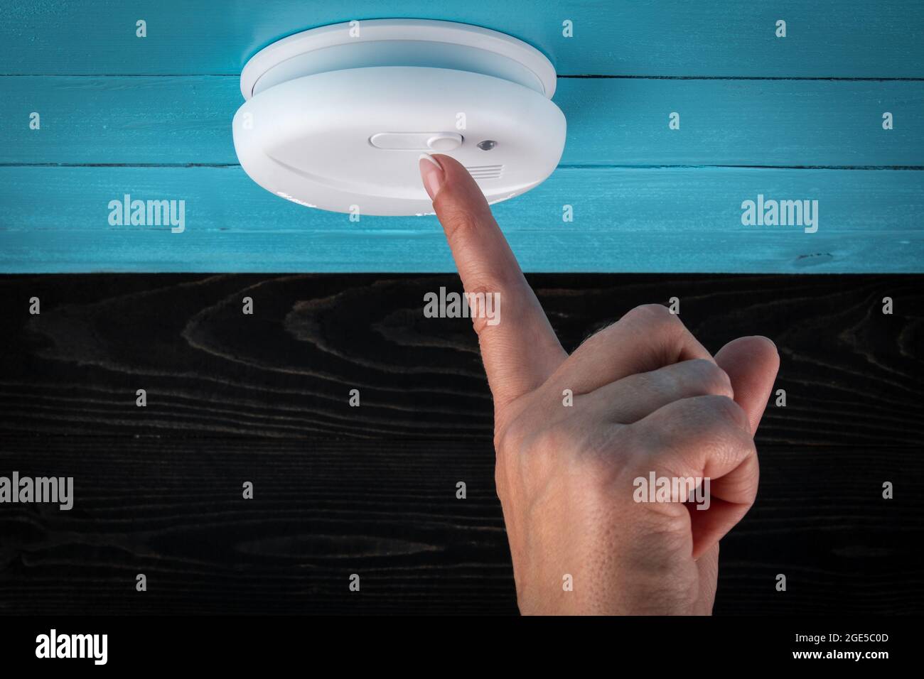 Close up smoke detector on a ceiling. Woman's finger presses the test button. Smoke, fire alarm