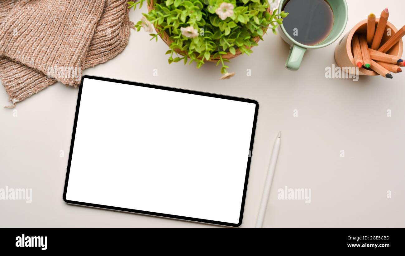 Trendy autumn workspace in natural white background with modern tablet screen mockup, stylus pen, knitted sweater, plant in pot, coffee, colour pencil Stock Photo